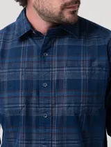 Camisa de manga larga para hombre, con estampado de cuadros tartán en tonos azul, gris y marrón. Presenta cuello clásico, cierre frontal de botones y dos bolsillos con solapa en el pecho.