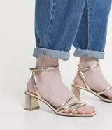 Sandalias doradas de tacón bloque, con tiras finas y cierre de hebilla en el tobillo.