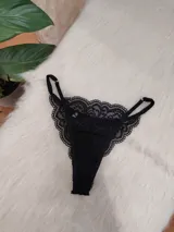 Tanga colaless de encaje negro con diseño floral, breteles regulables y herrajes metálicos.