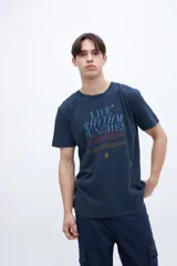 Remera de algodón color azul marino con cuello redondo y mangas cortas. Presenta un estampado gráfico central con texto en tonos azul claro, rojo y amarillo, incluyendo una pequeña estrella.