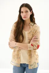 Camisa de tela liviana color beige, con bordados de corales en tonos azul, rojo y verde. Presenta un diseño ligeramente arrugado y botones blancos en el frente.