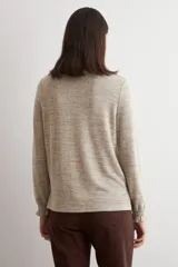 Remera de manga larga con cuello alto tipo media polera, confeccionada en tejido texturado de color beige melange, con puños con detalle de volados.