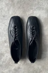 Zapatos planos de cuero negro con diseño de punta cuadrada y cierre de cordones al frente.