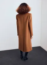 Abrigo largo de paño en color marrón, con diseño recto, cuello con solapas de muesca y cierre frontal de doble botonadura. Presenta mangas largas con puños abotonados y dos bolsillos laterales con solapa.