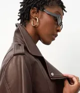 Campera estilo biker de cuero sintético color marrón chocolate, con cuello solapa, cierre asimétrico, bolsillos laterales con cremallera y detalles de botones metálicos. Incluye hombreras decorativas y puños estructurados.