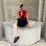 Cartera tipo tote bag confeccionada en lona de color negro. Presenta un diseño funcional con doble asa de mano, un compartimento principal espacioso y un bolsillo frontal con solapa.