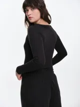 Remera de manga larga entallada en tejido pointelle, con escote bote y detalle de pequeño lazo central. Presenta un acabado con borde picot en el escote.