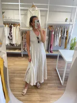 Vestido largo sin mangas, color beige claro, con escote en V y textura arrugada o arrugada, con terminación deshilachada en el ruedo.