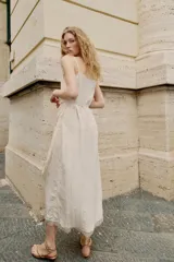 Vestido midi lencero de color blanco, confeccionado en tejido con efecto arrugado. Cuenta con escote recto, tirantes finos ajustables, diseño cruzado con cinturón fino para anudar y detalles de encaje en los acabados de la falda.