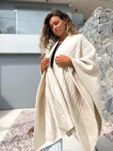 Ruana tejida en color crudo con diseño de trenzas y textura en relieve. Presenta un corte amplio y envolvente, ideal para usar como capa sobre otras prendas.