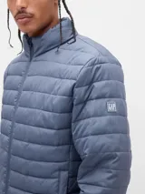 Campera puffer de diseño ligero, color verde militar, con cierre frontal completo y cuello alto. Presenta un acabado acolchado horizontal y puños elásticos.