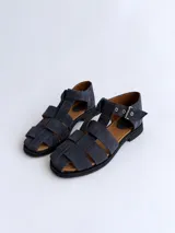 Sandalias cangrejeras de gamuza color marrón, con punta redonda, taco bajo, talonera cerrada y tira con hebilla metálica ajustable en el tobillo.