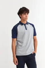 Remera polo de manga corta con diseño combinado, cuerpo en color gris melange y mangas junto con cuello en color azul marino. Presenta cierre frontal con botones y detalle de línea fina en el cuello.
