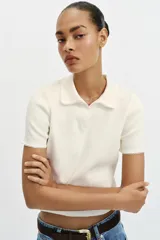 Top de punto color blanco marfil con cuello polo y manga corta. Presenta detalle de puntilla con forma de onda en el cuello y los puños.