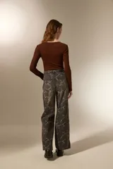 Pantalon de jean estilo baggy con estampado floral en tonos gris oscuro y blanco. Presenta un corte de pierna ancha, tiro medio y cierre frontal con botón y cremallera.