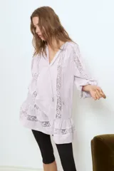 Vestido túnica corto de color lila en tejido de algodón con diseños bordados e inserciones de encaje. Modelo oversized con escote en V, cuello redondo con cordón y mangas raglán largas con elástico fino en los puños. Costura fruncida en la cadera con bajo acampanado.