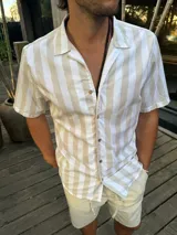 Camisa de manga corta con cuello cubano, confeccionada en tejido a rayas verticales en tonos arena y blanco, con cierre frontal de botones.