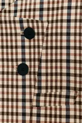 Blazer corto de cuello redondo y manga larga con estampado de cuadros. Presenta un diseño cruzado con cierre frontal de dos botones negros.