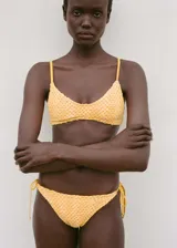 Top de bikini con diseño triangular confeccionado en tejido de crochet color amarillo, con forro interior y breteles finos.