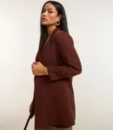 Blazer de sastrería color bordó, de corte oversized y largo, confeccionado en crepé. Presenta solapas clásicas, bolsillos frontales y detalle de pliegues en los puños.