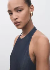Mono largo de denim oscuro con cuello halter y espalda descubierta. Presenta un diseño de corte recto y holgado con bolsillos laterales y cierre de cremallera en la parte posterior.