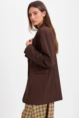 Blazer de corte sastrero en color marrón chocolate, con solapas clásicas, cierre frontal de un botón y bolsillos laterales con solapa.