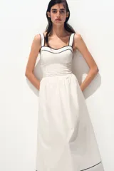 Vestido midi de algodón color blanco, con escote corazón, breteles anchos y espalda con punto smock. Presenta cuerpo entallado, costura fruncida en la cintura y pollera con vuelo, con ribetes negros en contraste en el escote y el bajo.