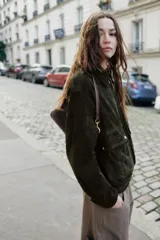 Cazadora de piel ante color verde oscuro, con cuello solapa, manga larga con trabillas en los hombros, bolsillos delanteros de plastrón con solapa y botones a presión, bajo elástico y cierre frontal con cremallera.