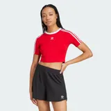 Remera corta roja ajustada al cuerpo, de manga corta, con cuello redondo blanco y las icónicas tres líneas blancas de Adidas en las mangas. Cuenta con el logo del trifolio bordado en el pecho.