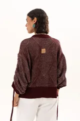 Buzo de punto color vino con diseño de trama geométrica, cuello redondo, mangas largas con puños ajustables mediante cordones y terminaciones acanaladas.