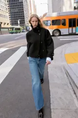 Abrigo corto de paño en color negro, con cuello subido, cierre frontal cruzado con botones, mangas largas con trabillas en los puños y bolsillos delanteros de vivo.