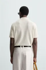 Polo negro de manga corta con cuello solapa y abertura frontal. Presenta un tejido jacquard con textura geométrica sutil.