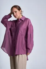 Camisa negra de tela traslúcida con cuello clásico, cierre frontal con botones y dos bolsillos de parche en el pecho.