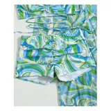 Conjunto de traje de baño de tres piezas con estampado de hojas tropicales en tonos blanco y negro. Incluye un top tipo tankini con cordón ajustable en el centro, un short de tiro alto y una camisa abierta de manga larga tipo salida de baño.