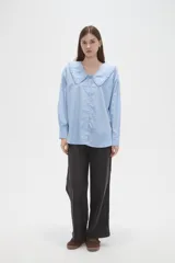 Camisa de algodón color celeste, con cuello grande tipo babero con volados, cierre frontal con botones y mangas largas con puños.