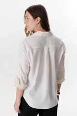 Camisa verde militar de manga larga con puños color crema, cuello clásico y cierre frontal con botones. Tiene un bolsillo en el pecho con bordado de una palmera color crema.