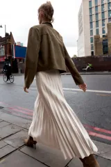 Falda midi plisada de tiro alto color beige, con cinturón a tono y hebilla metálica dorada. Cierre lateral con cremallera oculta.