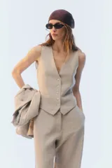 Chaleco sastrero color beige, con escote en V y cinco botones frontales.