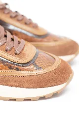 Championes deportivos en tonos marrón y caramelo con estampado de serpiente y detalles en charol. Cuenta con cordones marrones y suela de goma blanca con base dentada.