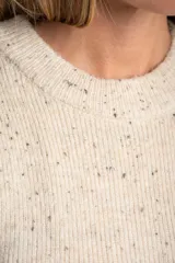 Chaleco de punto sin mangas en color beige melange con motas oscuras. Presenta cuello redondo y terminaciones acanaladas en el ruedo y las sisas.