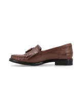 Mocasín de cuero color marrón cognac con detalle de flecos y borlas en el empeine, costuras pespunteadas y suela plana con pequeño tacón.