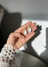 Aros colgantes con forma de trébol de cuatro hojas con circonitas verdes y perla barroca de río. El metal es plata 925 con baño de oro.