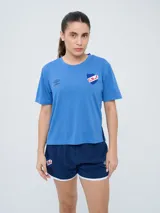 Remera de fútbol Umbro del Club Nacional de Football, modelo Bink para mujer. Diseño azul oscuro con cuello redondo y mangas cortas, con logo de Umbro en el pecho derecho y escudo del club en el pecho izquierdo.