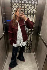 Campera de tela bouclé color bordó, con diseño de cuello redondo y cierre frontal mediante botones. Presenta detalles de volados en tela agamuzada en el pecho y en las mangas.