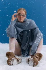 Sweater de punto en color azul grisáceo con diseño oversize. Presenta cuello redondo, mangas largas y detalles de estampados gráficos en el frente y en una de las mangas. El tejido posee un acabado desgastado que le otorga un aspecto vintage.