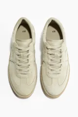 Zapatillas deportivas color beige con collarín acolchado, lengüeta y cierre de cordones. Suela texturizada gruesa con diseño.