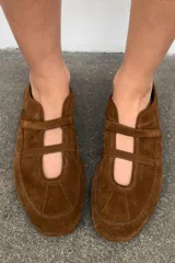 Bailarina deportiva de serraje color marrón, con diseño de doble tira en el empeine, una elástica y otra con cierre adhesivo. Presenta costuras decorativas en el cuerpo, suela plana y punta redonda.