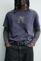 Camiseta de corte relajado con cuello redondo y manga corta. Presenta un acabado con efecto lavado que le otorga una apariencia única y desgastada. Incluye estampados a contraste en la parte frontal.