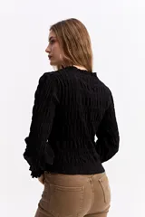 Blusa negra de algodón con textura fruncida en todo el cuerpo, cuello alto y puños con volados.