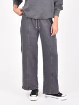 Pantalón ancho de tela tipo jogging, color gris oscuro con efecto lavado o acid wash. Presenta costuras marcadas verticales en el frente de cada pierna y cintura ajustable con cordón.